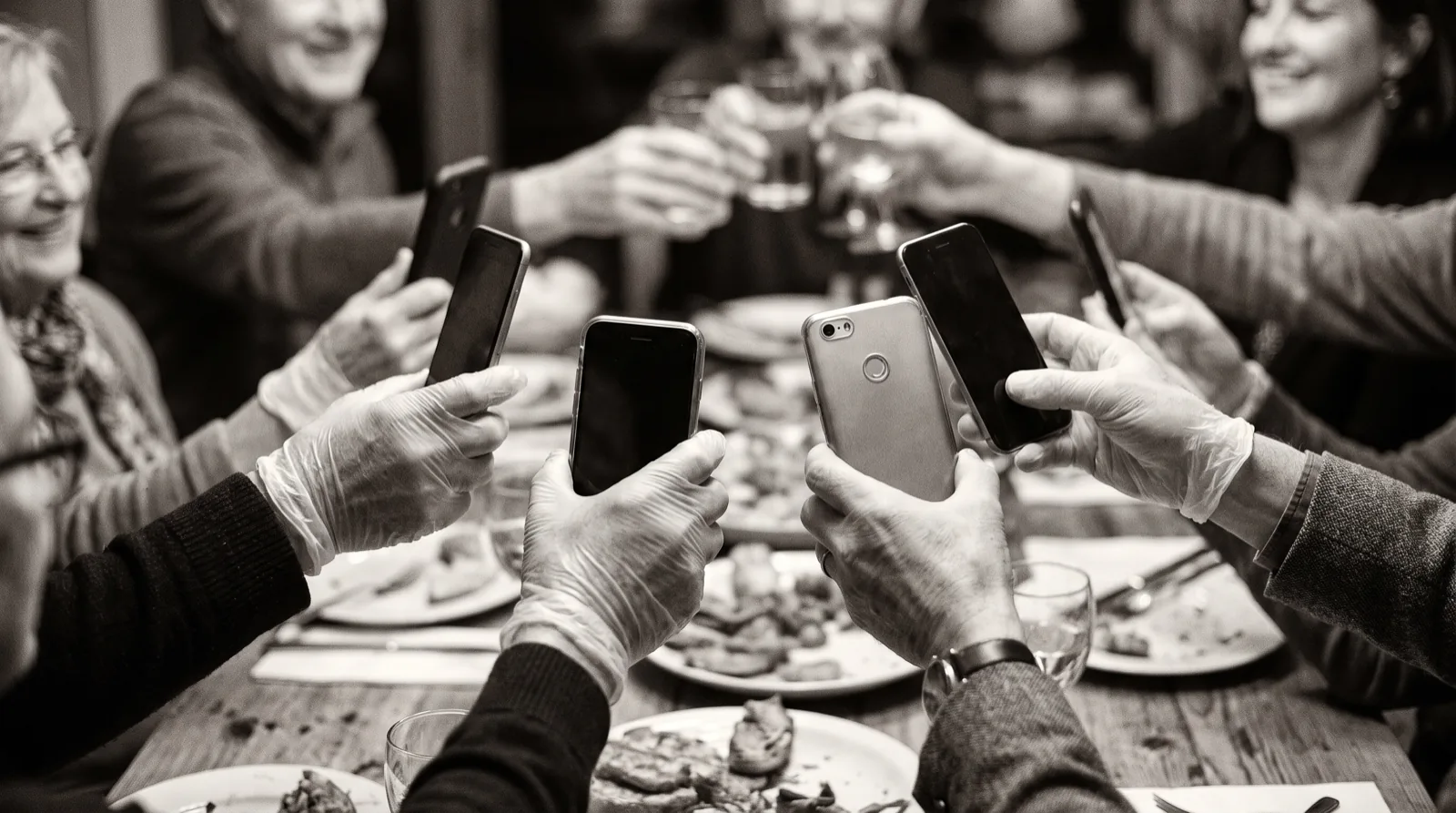 Mehrere Hände halten Telefone unterschiedlicher Bauart über einen Tisch, alle Bildschirme abgewandt.