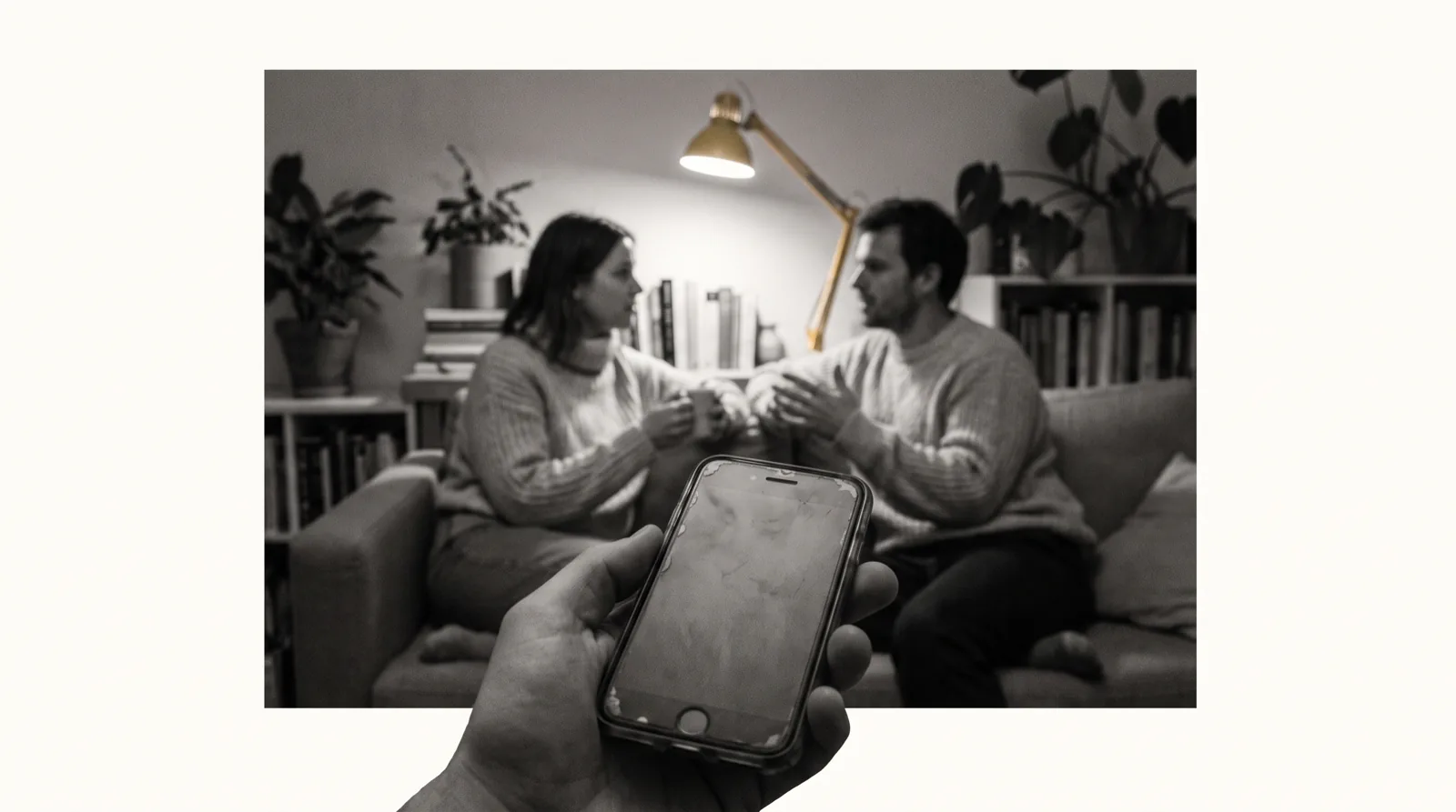 Eine Hand hält ein Telefon, im Hintergrund unscharf ein Wohnzimmer mit Gästen.