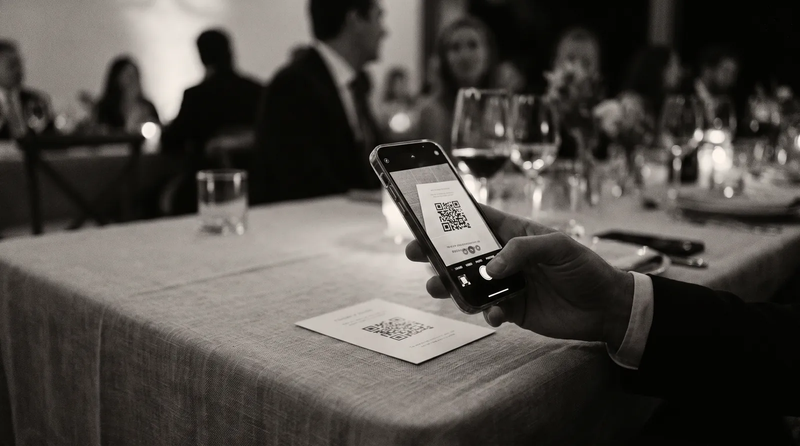 Eine Hand hält ein Telefon über eine gedruckte Tischkarte, die Kamera zeigt deren QR-Code im Sucher.