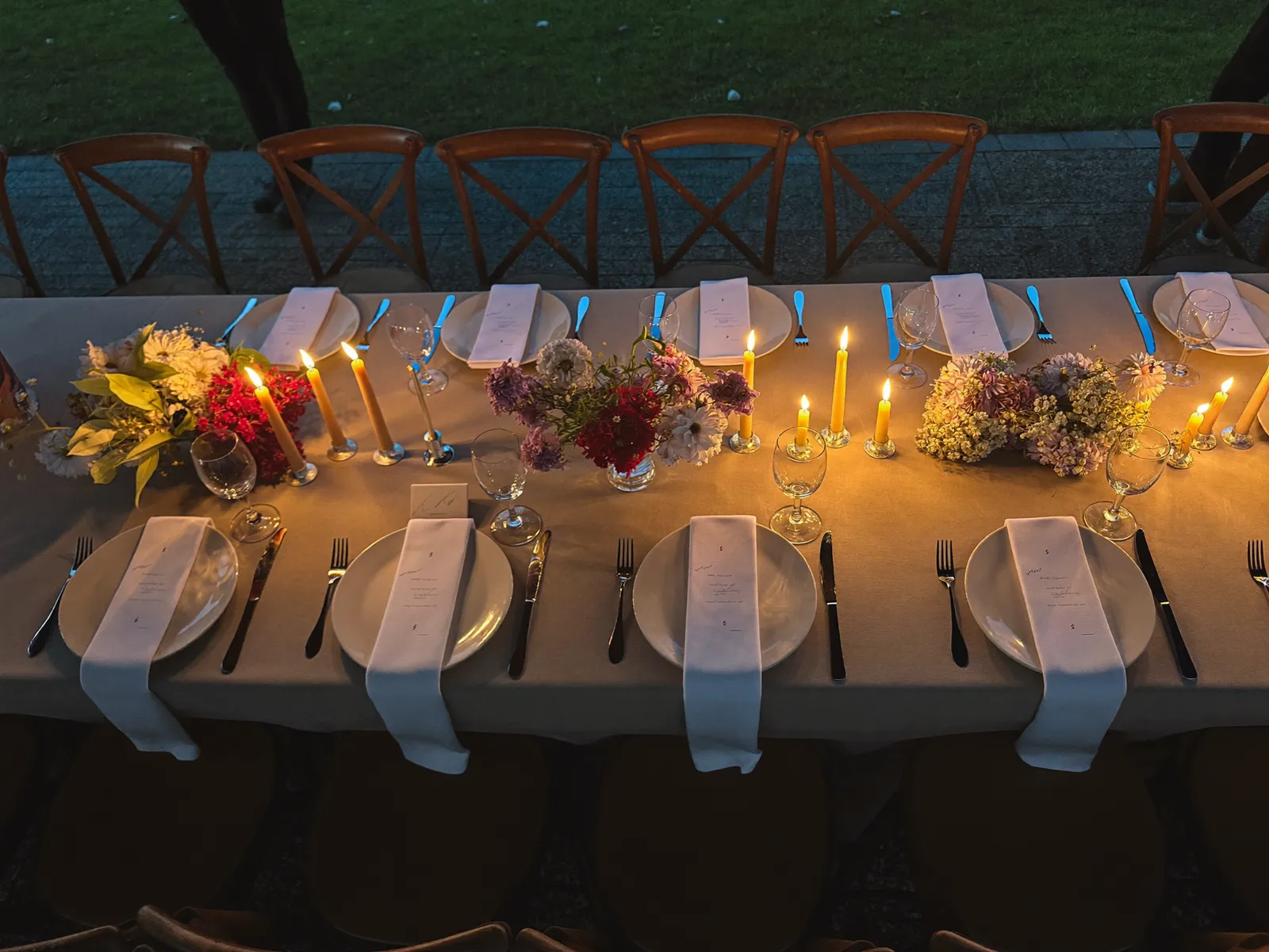 Langer gedeckter Tisch in der Dämmerung mit Kerzen, Blumen und Menükarten